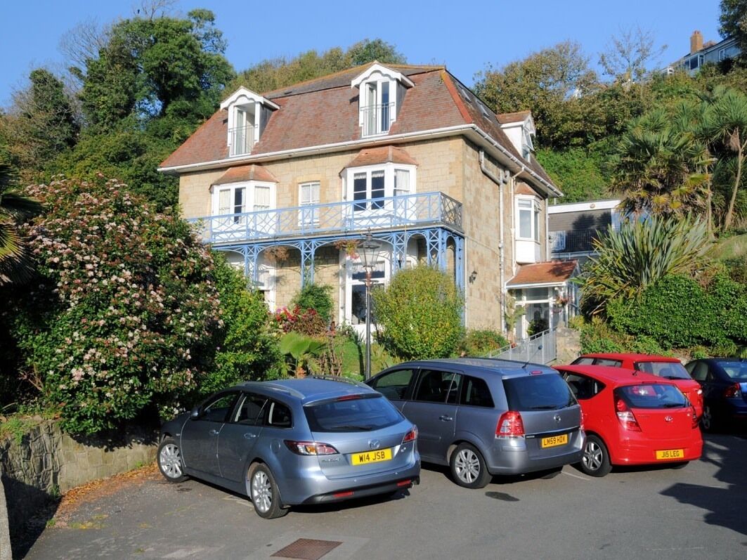 A two-story building with a balcony, parked cars, and lush greenery.