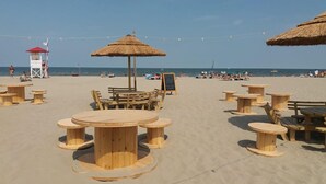 A beachside café with wooden tables and thatched umbrellas, a lifeguard tower, and the ocean in the background. - Michelangelo Holiday & Family Resort (Comacchio)