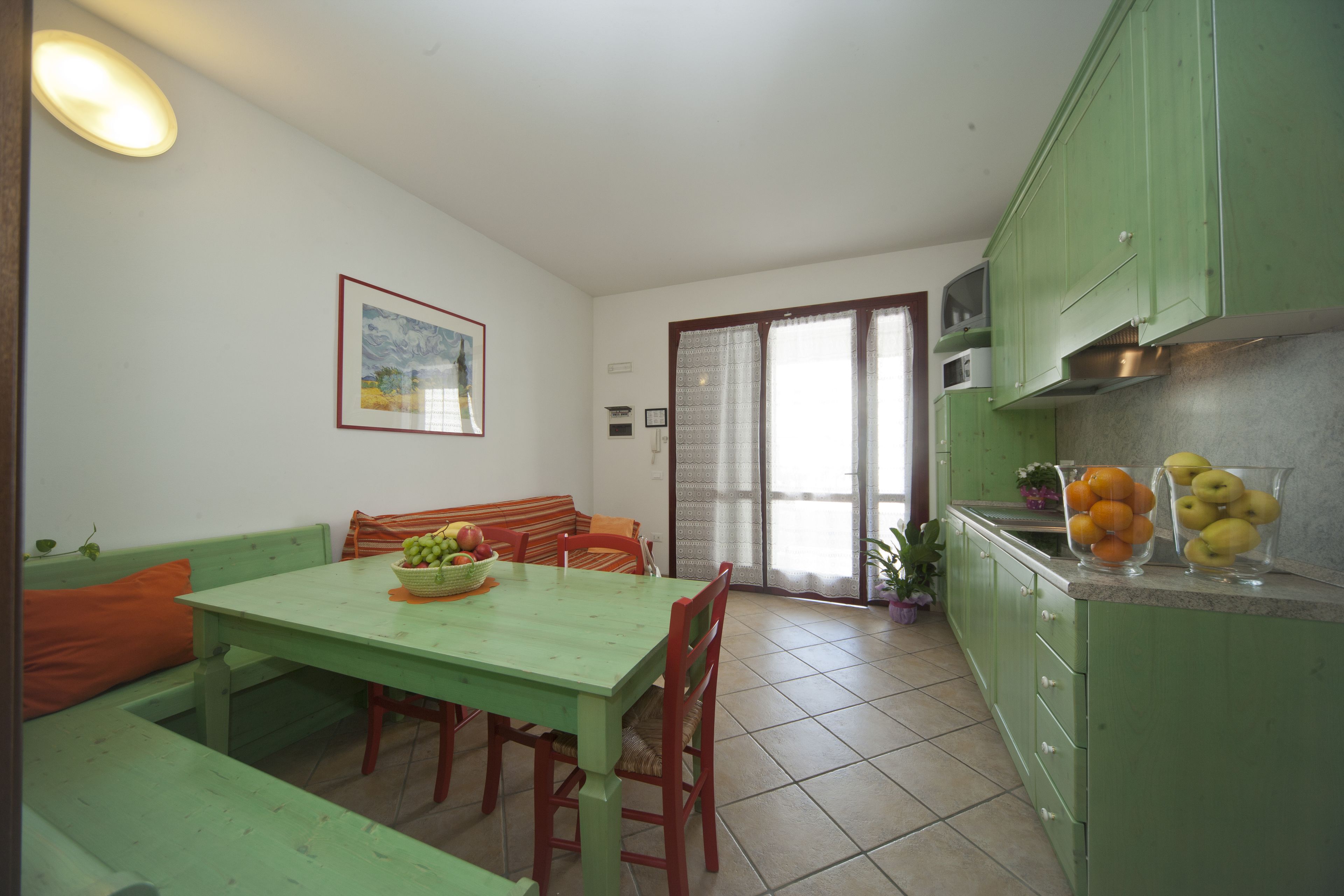 A dining area with a green table and chairs, a bench, and a kitchen with green cabinets and a microwave.