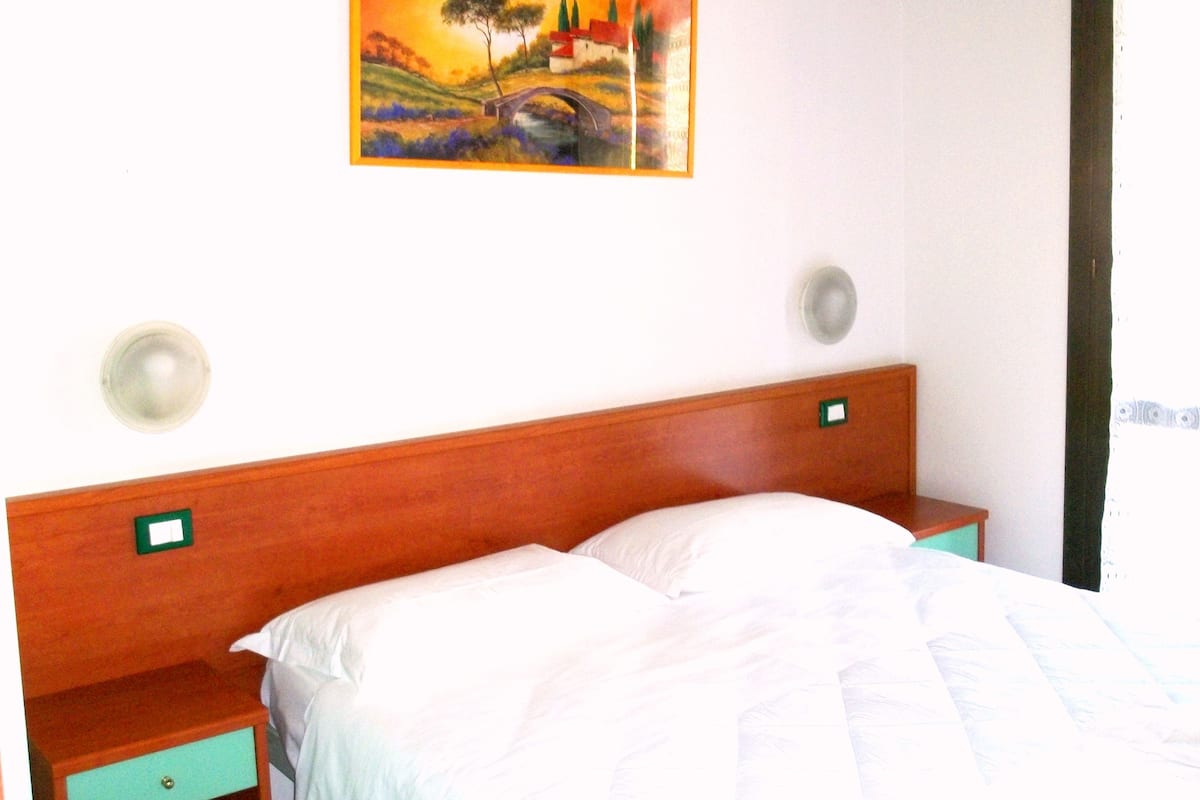 A hotel room with a wooden headboard, a bed with white bedding, two bedside tables, and a painting on the wall.
