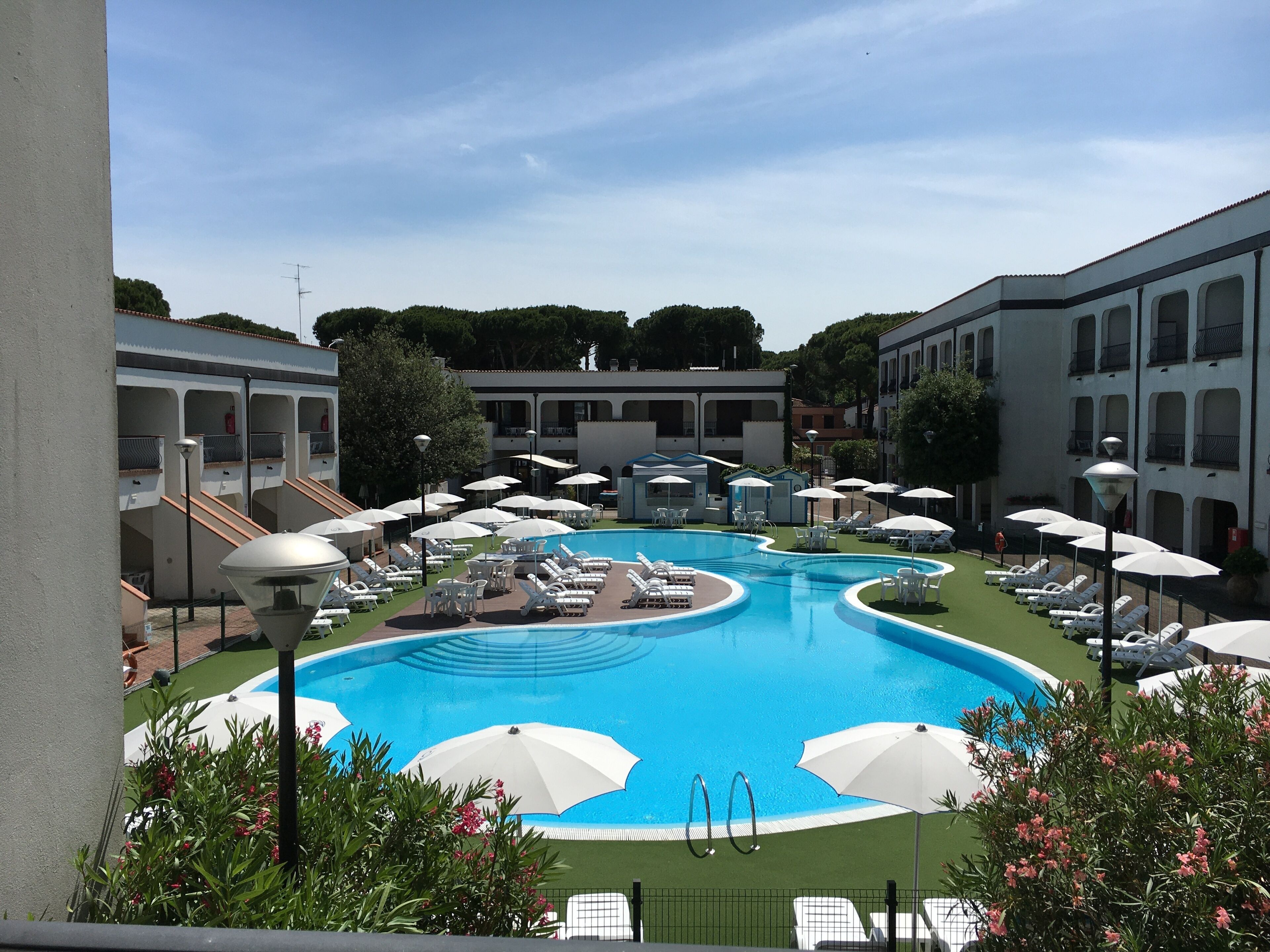 A swimming pool surrounded by lounge chairs and umbrellas, with buildings in the background.