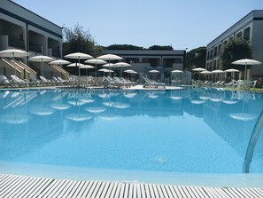 A swimming pool with lounge chairs and umbrellas, surrounded by buildings. - Michelangelo Holiday & Family Resort (Comacchio)