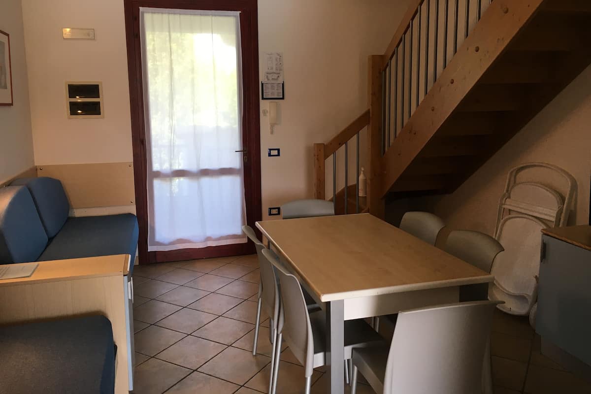 A small, cozy room with a wooden table, two chairs, a sofa, and a staircase.