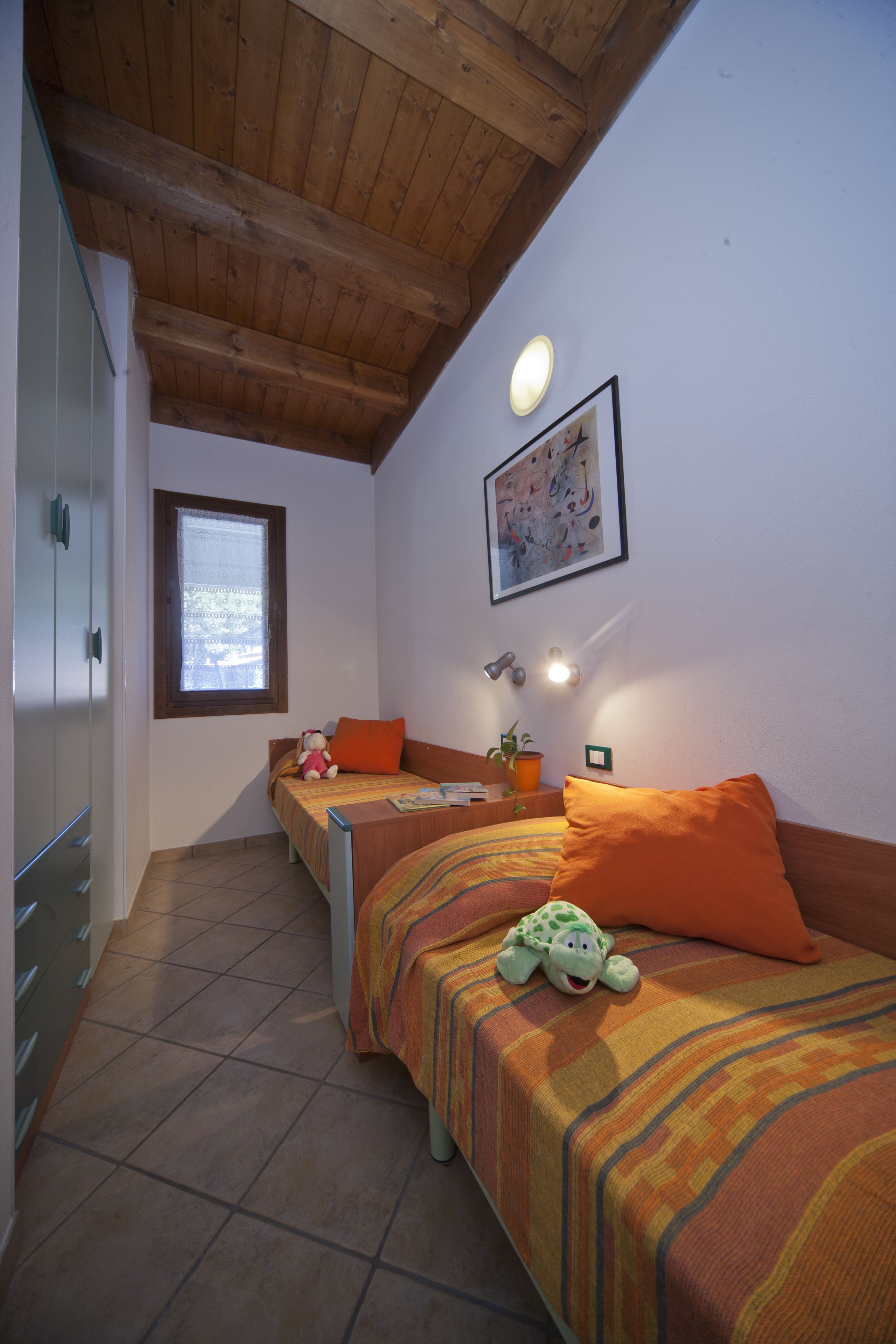 Un dormitorio con dos camas, una ventana, un ventilador de techo y una lámpara fijada a la pared.