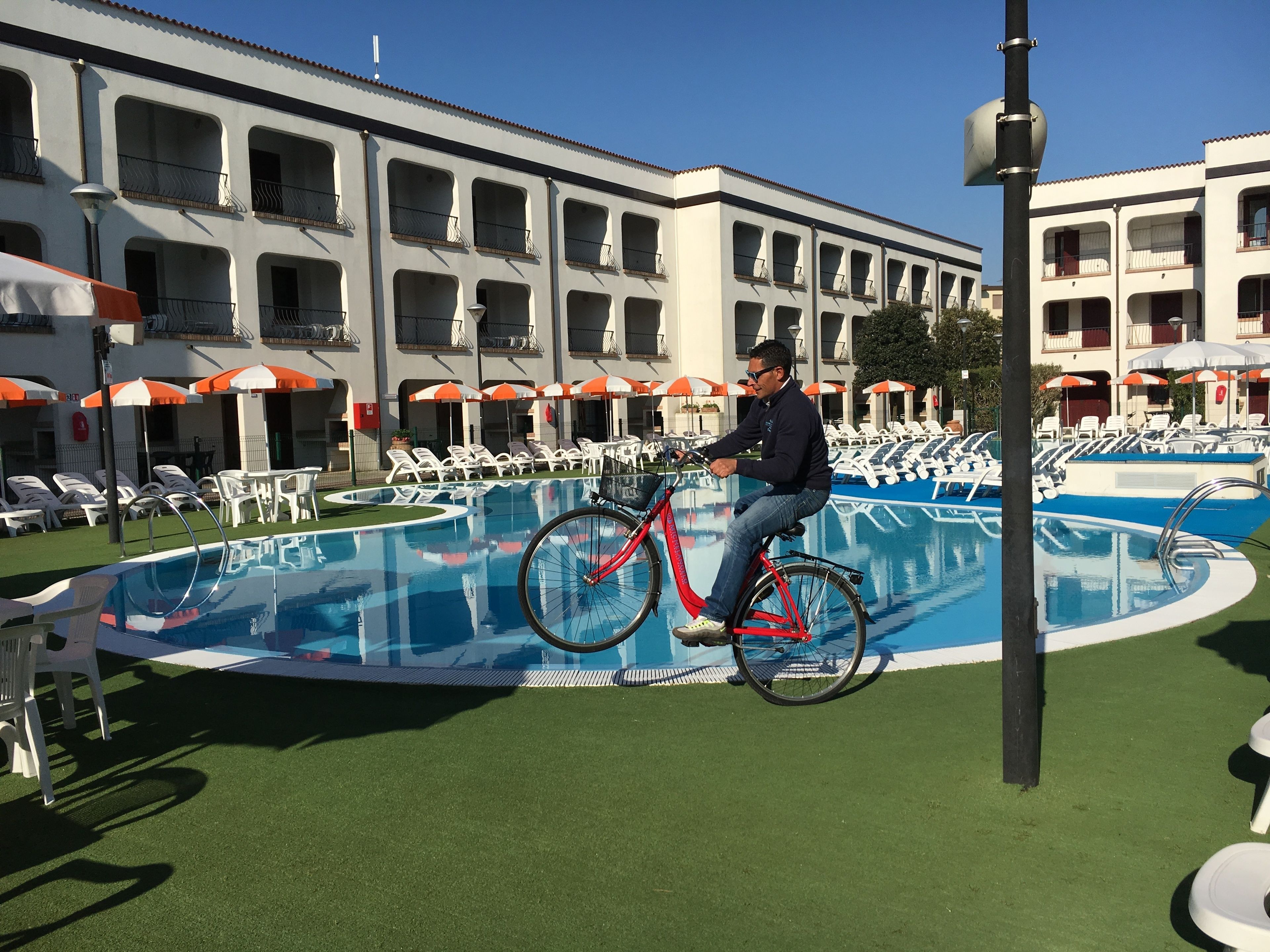 Een man fietst vlakbij een zwembad met ligbedden en parasols.
