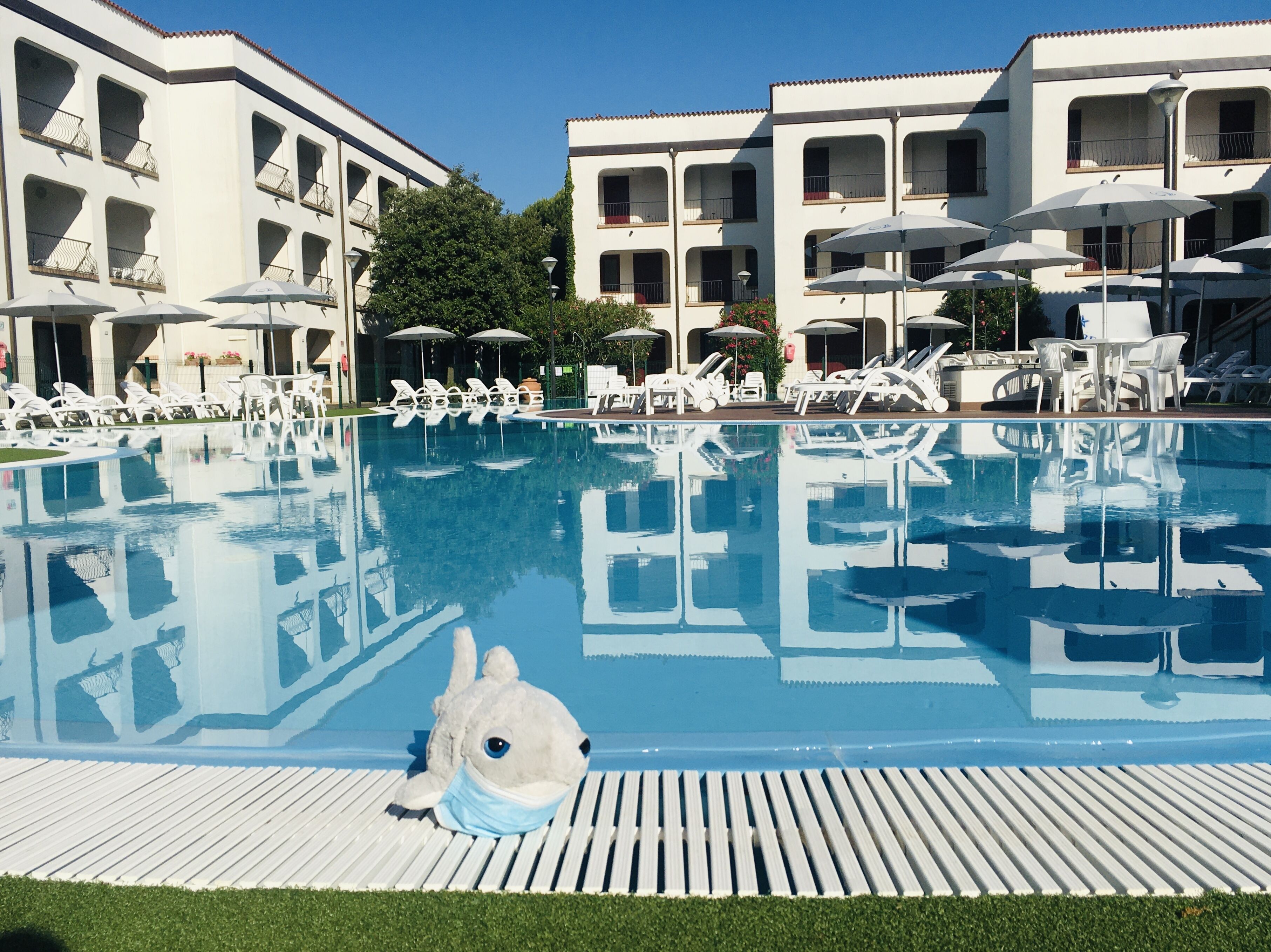 A swimming pool with lounge chairs and umbrellas, surrounded by multi-story buildings with balconies.