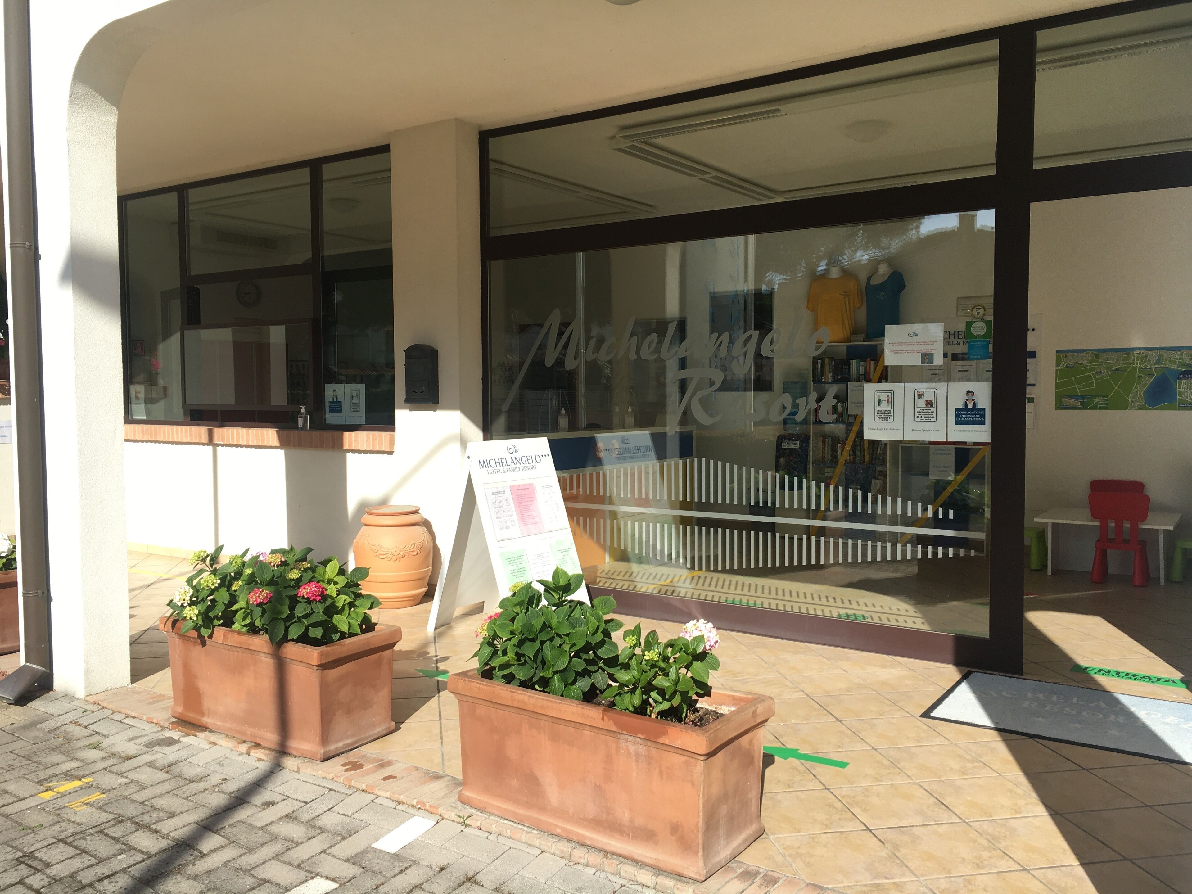 A hotel entrance with terracotta planters, a welcome sign, and a view of the interior through large windows.