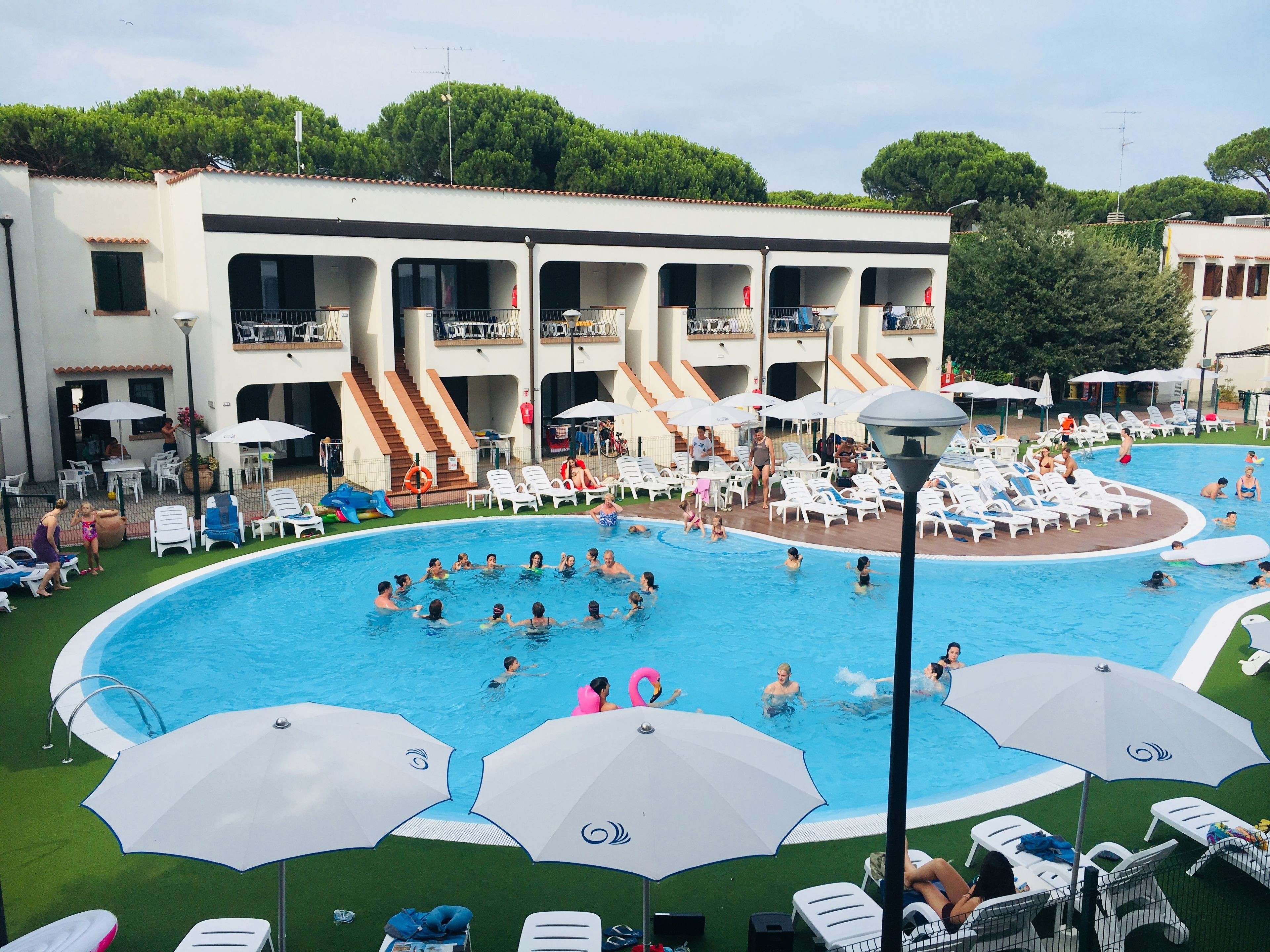 A swimming pool with multiple levels of balconies, surrounded by lounge chairs and umbrellas.