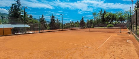 A tennis court with a net, surrounded by trees and a fence.