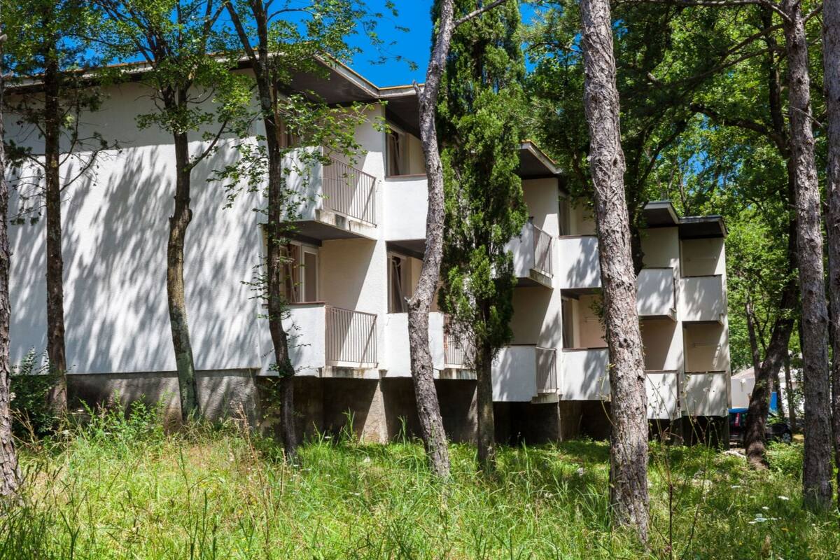 Un edificio de varios pisos con balcones, rodeado de árboles.