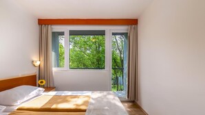Una habitación de hotel con dos camas, una ventana con cortinas, una mesita de noche con una lámpara y un girasol sobre la mesita.