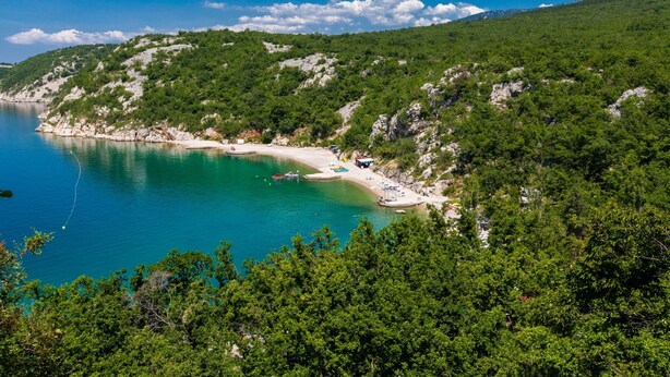 Zona costera con playa, embarcaciones y un promontorio rocoso.