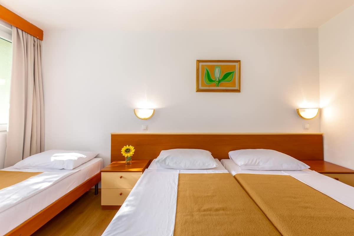 Una habitación de hotel con dos camas, cabecero de madera, mesita de noche con un jarrón de flores y lámparas de pared.