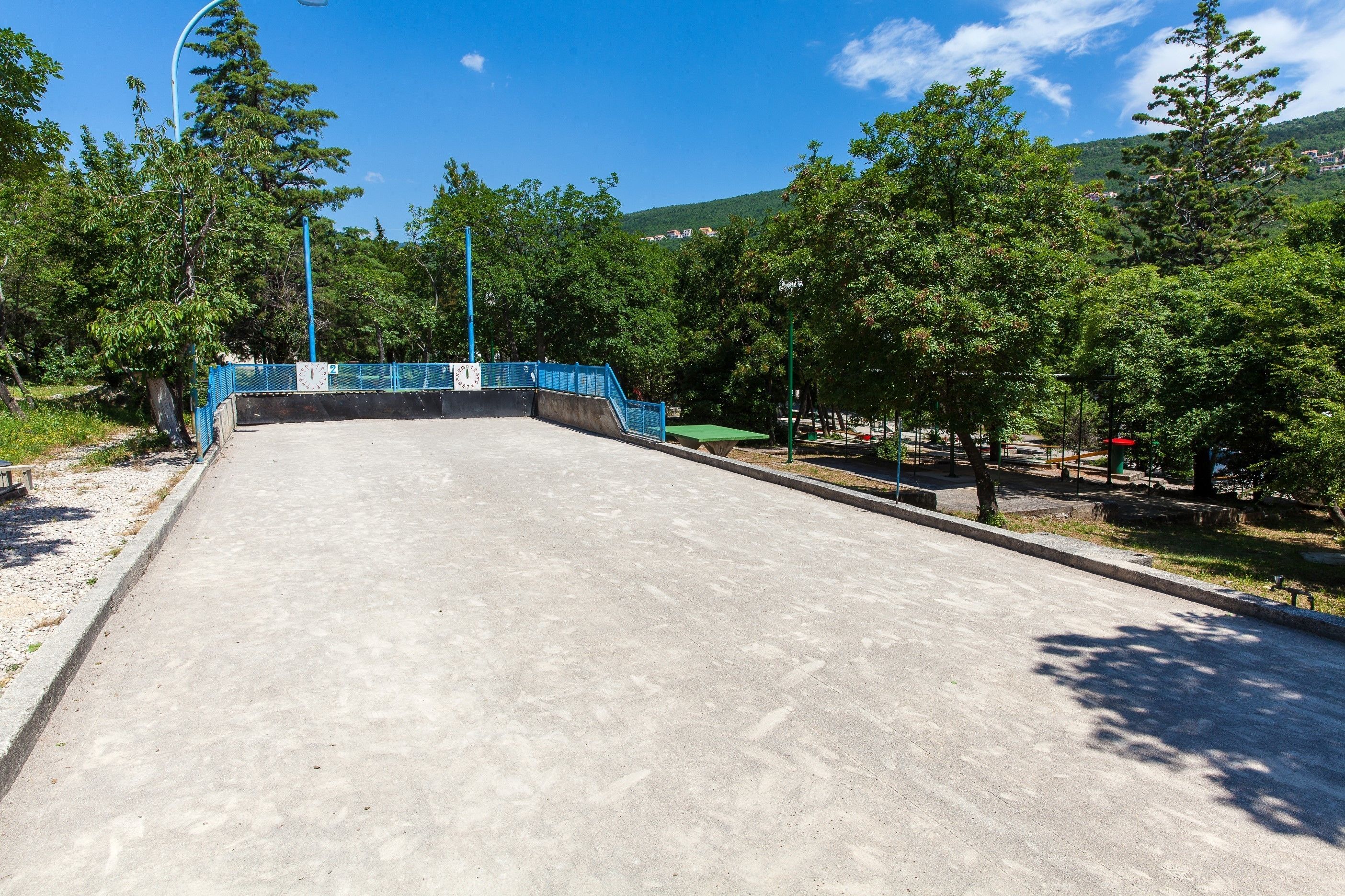 An outdoor area with a concrete surface, surrounded by trees and a blue railing.