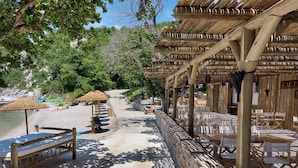 Zona de playa con pérgolas de madera, muros de piedra y sillas de playa.