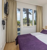 Una habitación de hotel con cama, televisión montada en la pared, teléfono y ventana con cortinas.