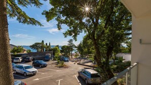 A parking area with several cars, a tree, and a view of the sea. - Hotel Slaven (Crikvenica)