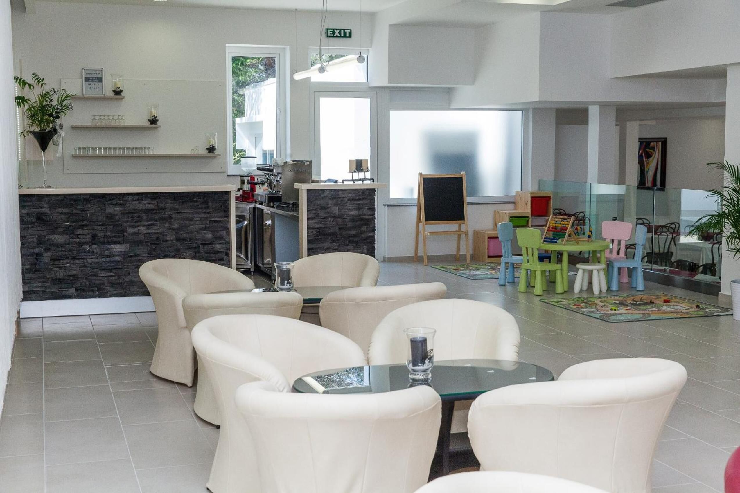 A modern hotel lobby with a reception desk, seating area, children's play area, and a large window providing natural light.