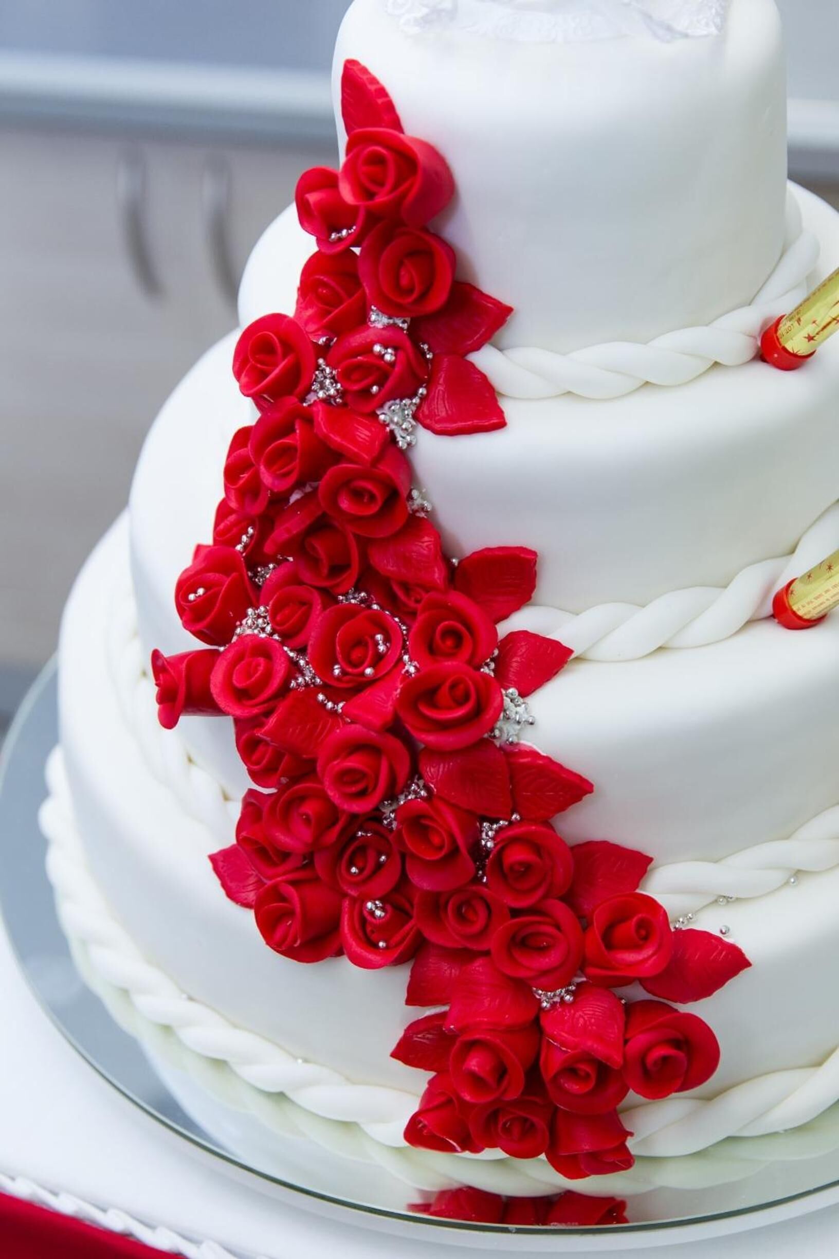 A white cake with red roses and a bottle of champagne.