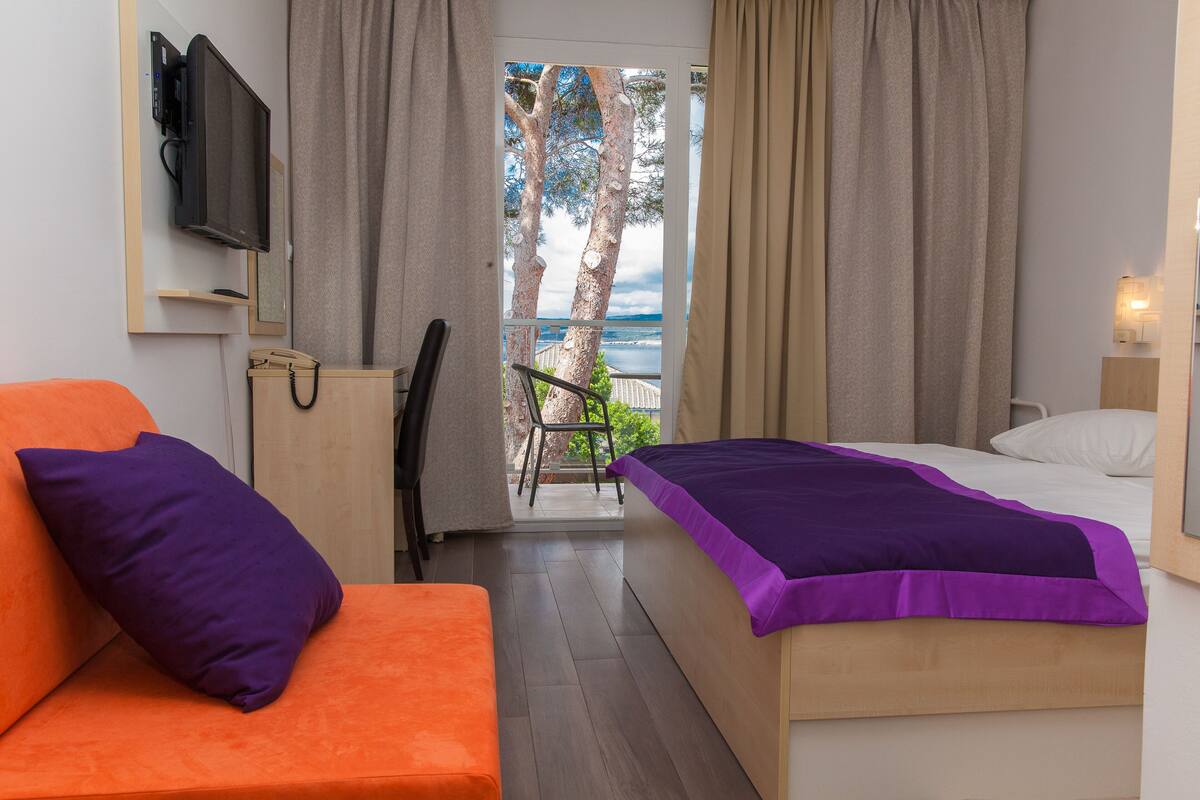 A bedroom with a bed, a sofa, a TV, and a view of the sea.