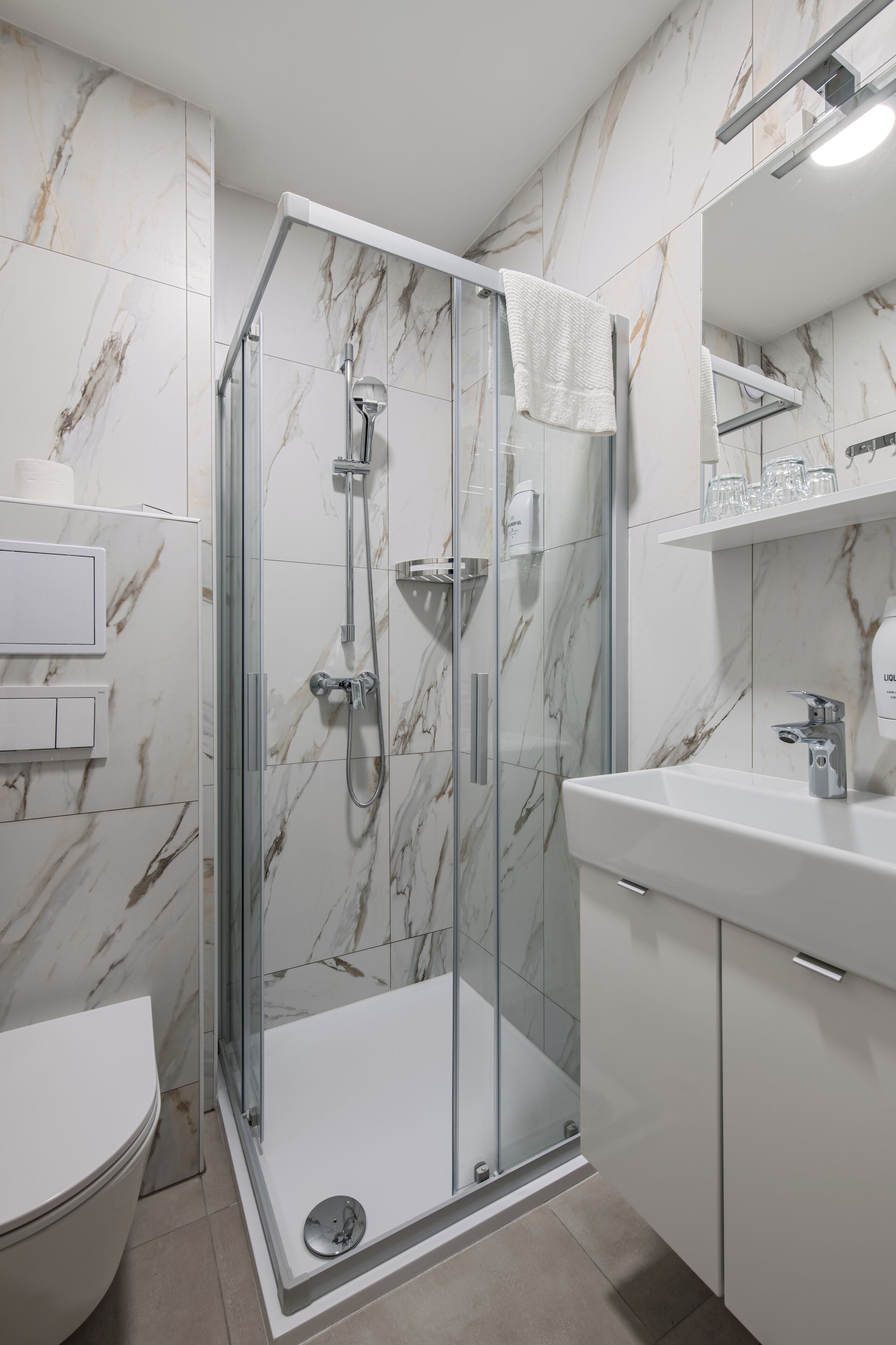 A modern bathroom with a glass-enclosed shower, white marble walls, and a white sink with a mirror above it.