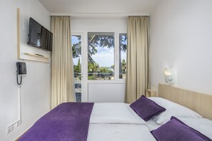 Habitación de hotel con cama, televisión montada en la pared, teléfono y ventana con cortinas.