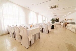 Un comedor amplio con varias mesas cubiertas de manteles blancos, dispuestas en fila.