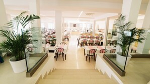 A spacious indoor dining area with multiple tables and chairs, potted plants, and a central staircase. - Hotel Slaven (Crikvenica)
