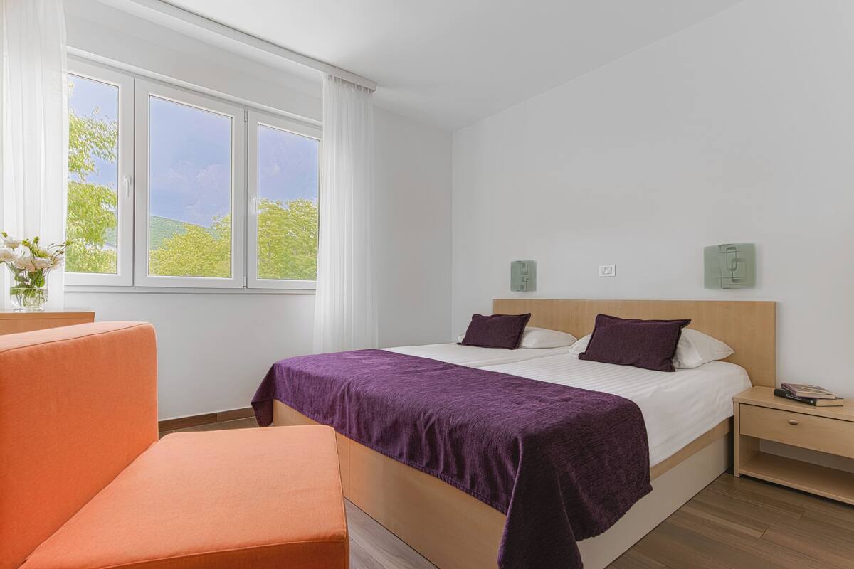 A hotel room with a bed, a nightstand, a chair, and a window with curtains.