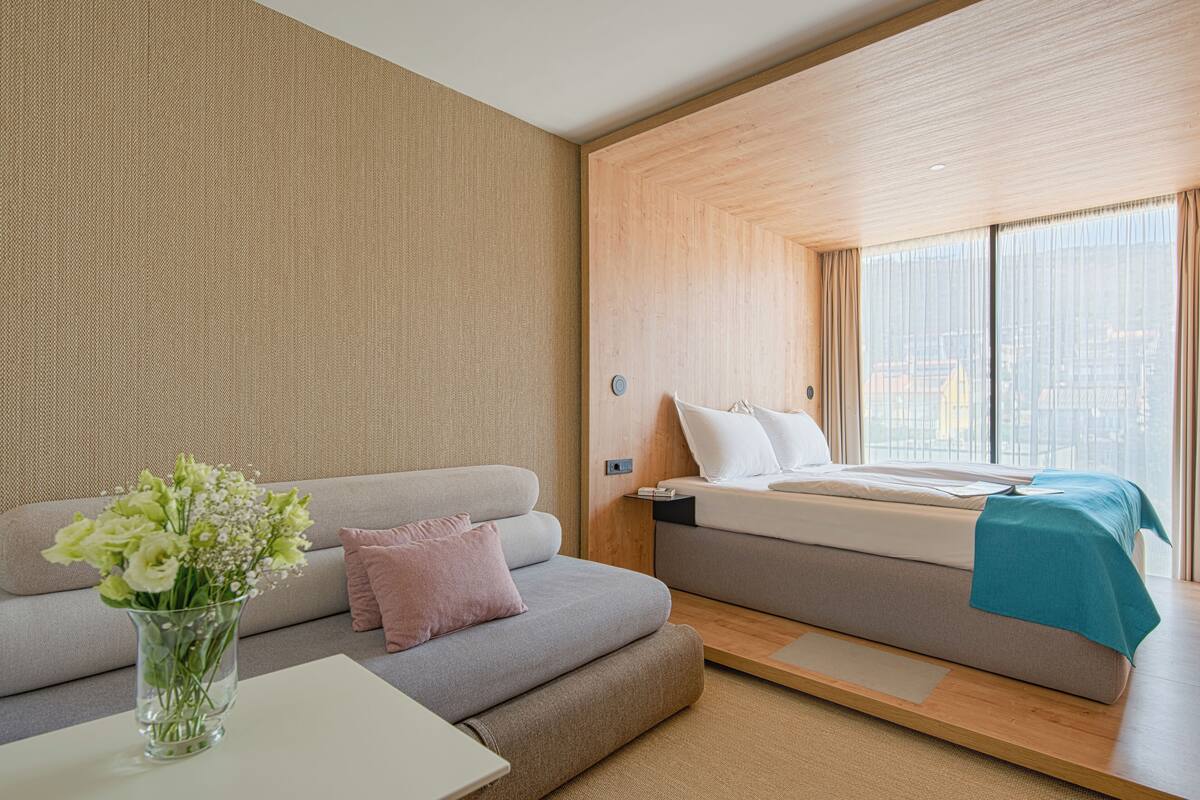 A modern hotel room with a sofa, a bed, and a vase of flowers.