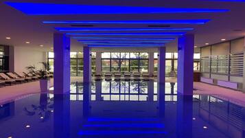 Un área de piscina interior moderna, con vista despejada a la piscina, sillas de descanso y una pared de vidrio que ofrece vistas al exterior.