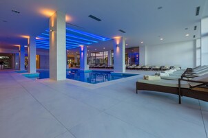 Area piscina interna moderna con più piscine, sedie a sdraio e un angolo relax vista piscina.