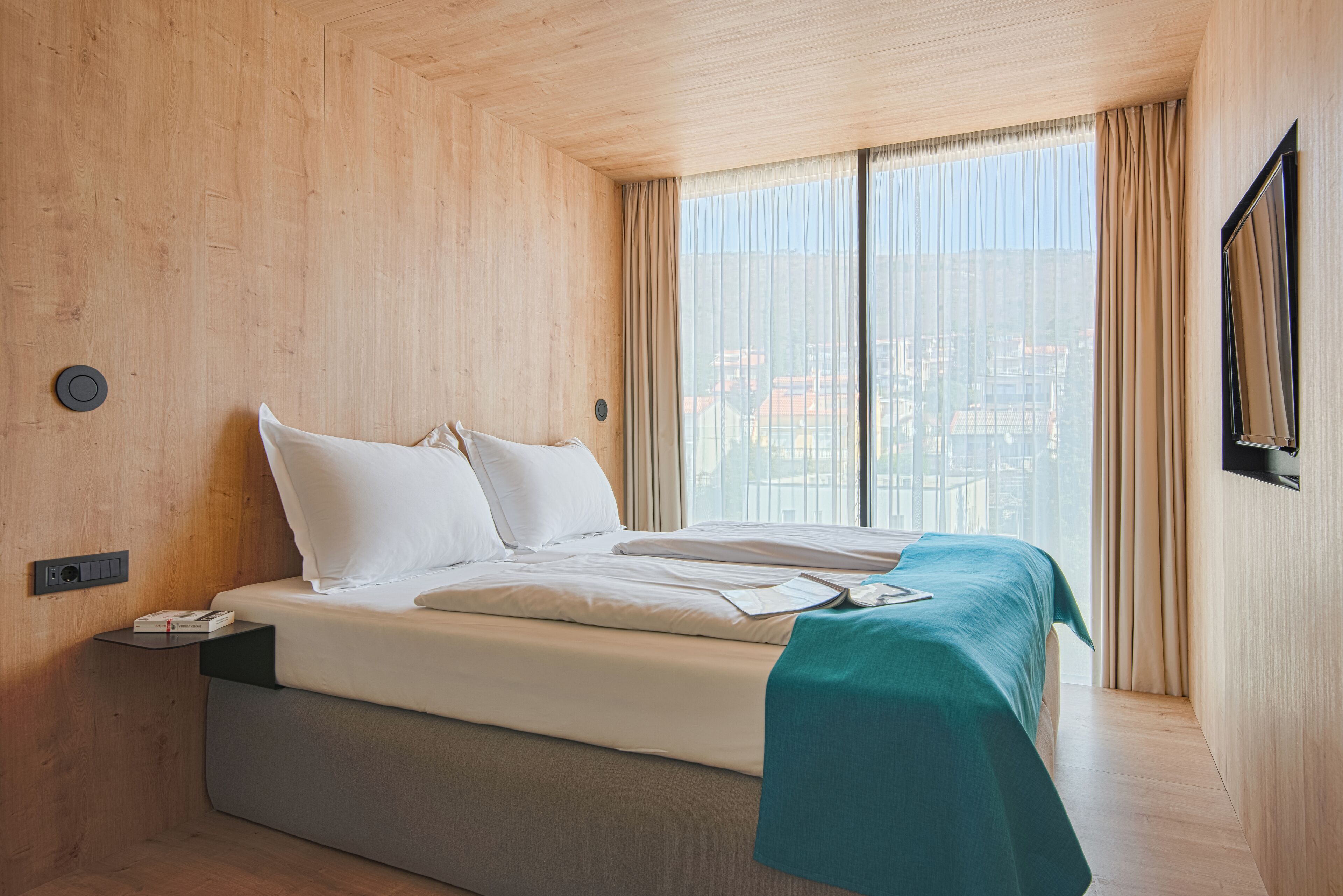 A modern hotel room with a large bed, a view of the city, and a wooden interior.
