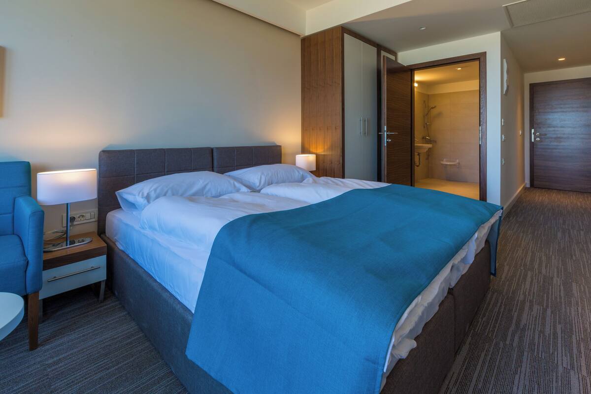 A hotel room with a bed, a nightstand, a chair, and a bathroom visible through an open door.