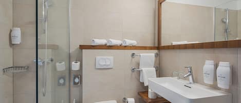 Un baño moderno con cabina de ducha de vidrio, inodoro blanco, lavamanos con dispensadores de jabón y espejo sobre el lavamanos.