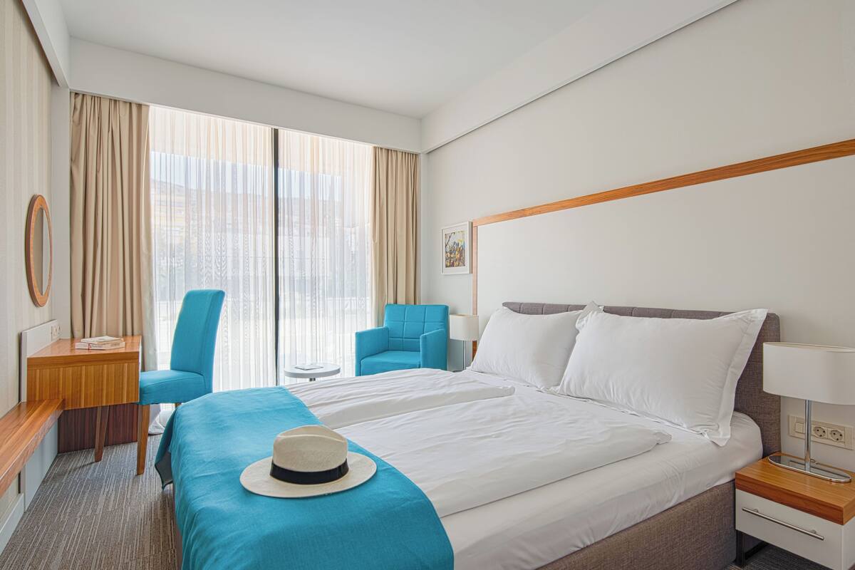 A hotel room with a large bed, a desk, a chair, and a view of the city through the window.