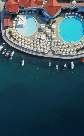 An aerial view of a resort with two large swimming pools, a marina with boats, and sun loungers arranged around the pools. - Hotel Katarina (Crikvenica)