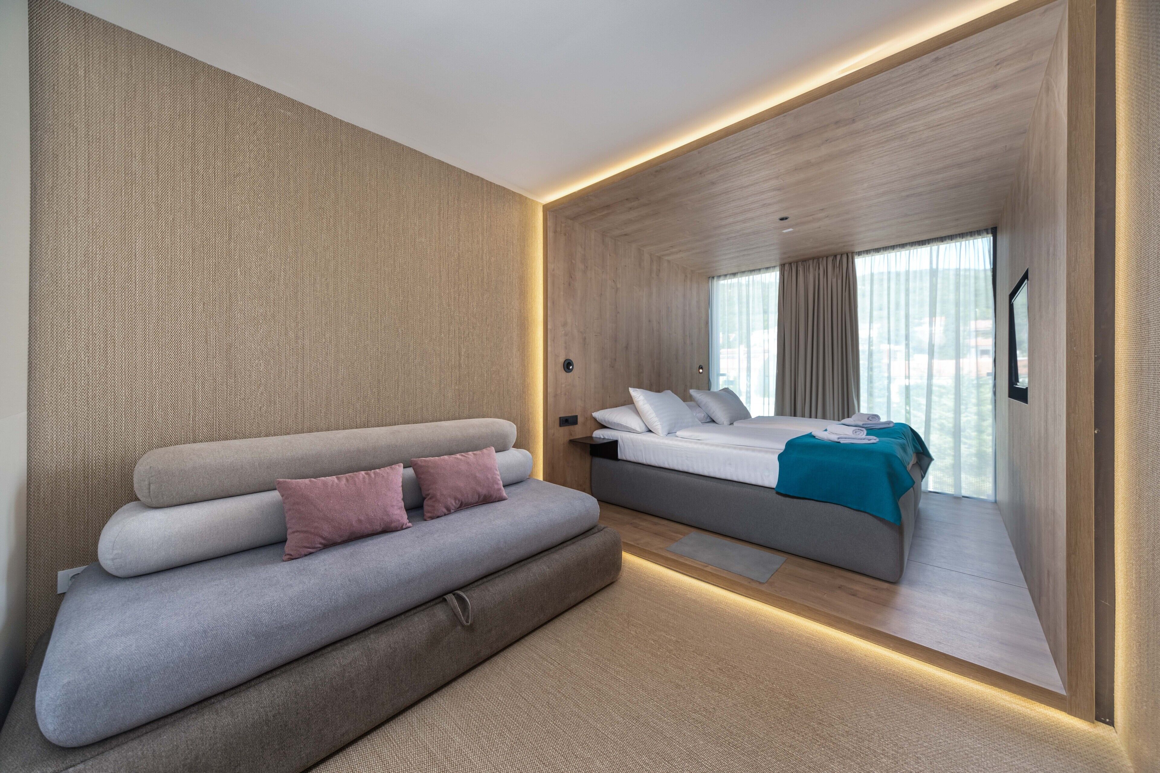 A modern hotel room with a sofa, a bed, and a large window.