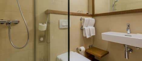 A modern bathroom with a glass-enclosed shower, a white toilet, a wooden vanity with a sink, and a mirror above the sink.