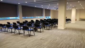 A conference room with rows of chairs, large windows, and a carpeted floor.