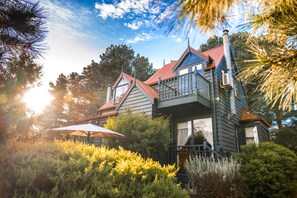 A two-story house with a balcony, surrounded by lush greenery and a red roof. - Bells Estate Great Ocean Road Cottages (Bellbrae)