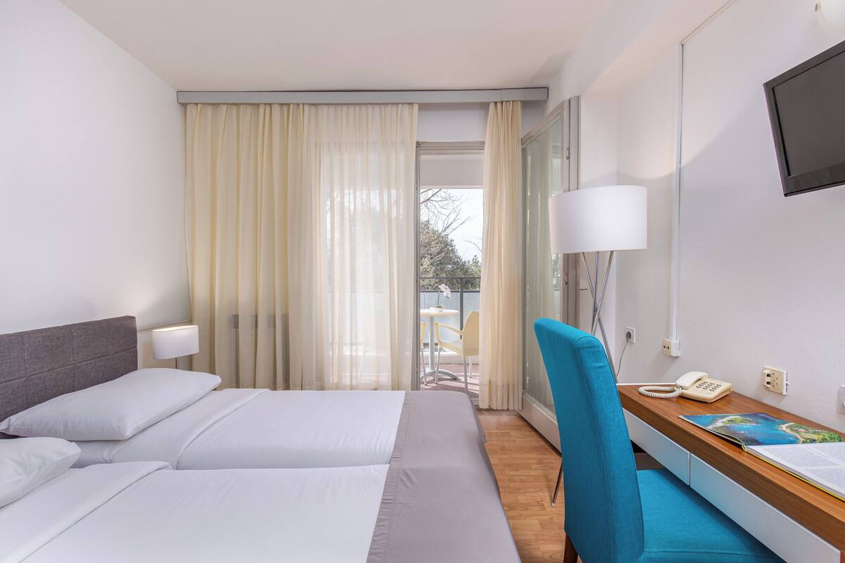 A hotel room with a bed, a desk with a lamp, a chair, a phone, and a TV on the wall.