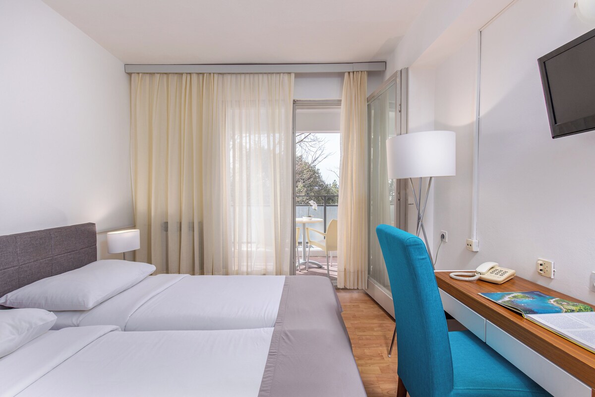 Une chambre d’hôtel avec un lit, un bureau doté d’une lampe, une chaise, un téléphone et un téléviseur fixé au mur.