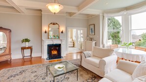 A spacious living room with a fireplace, white sofas, a glass coffee table, and a large window with curtains. - Fairholme Manor (Victoria)