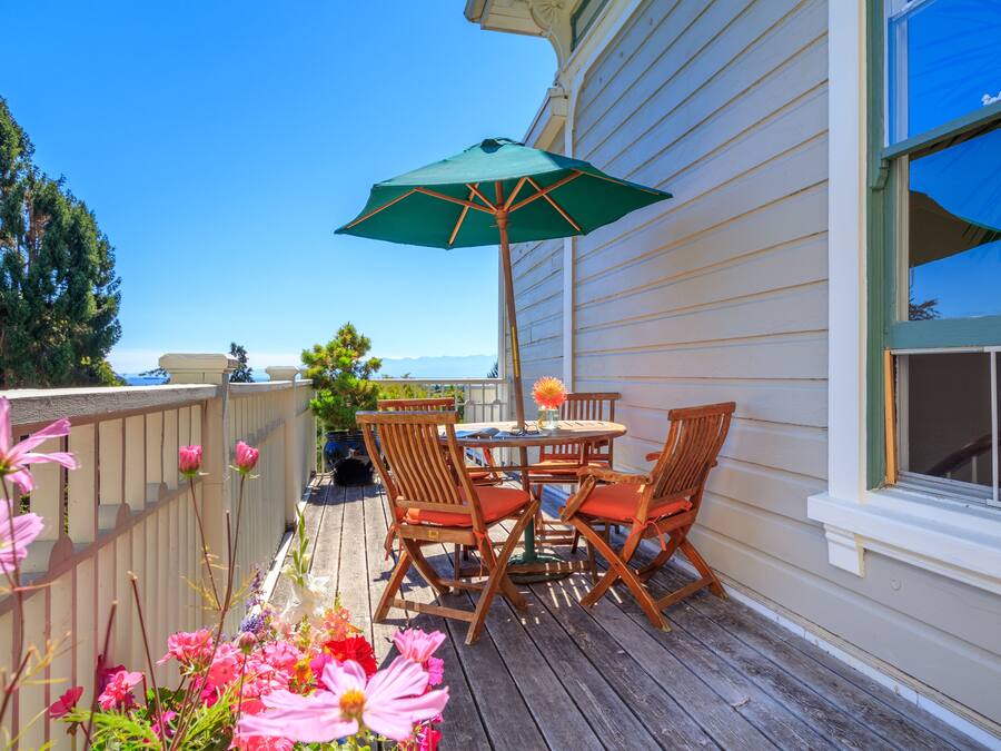 A wooden deck with a table and chairs, a green umbrella, and a flower arrangement.