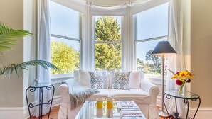 A cozy room with a white sofa, a glass coffee table, and a view of trees through large windows. - Fairholme Manor (Victoria)