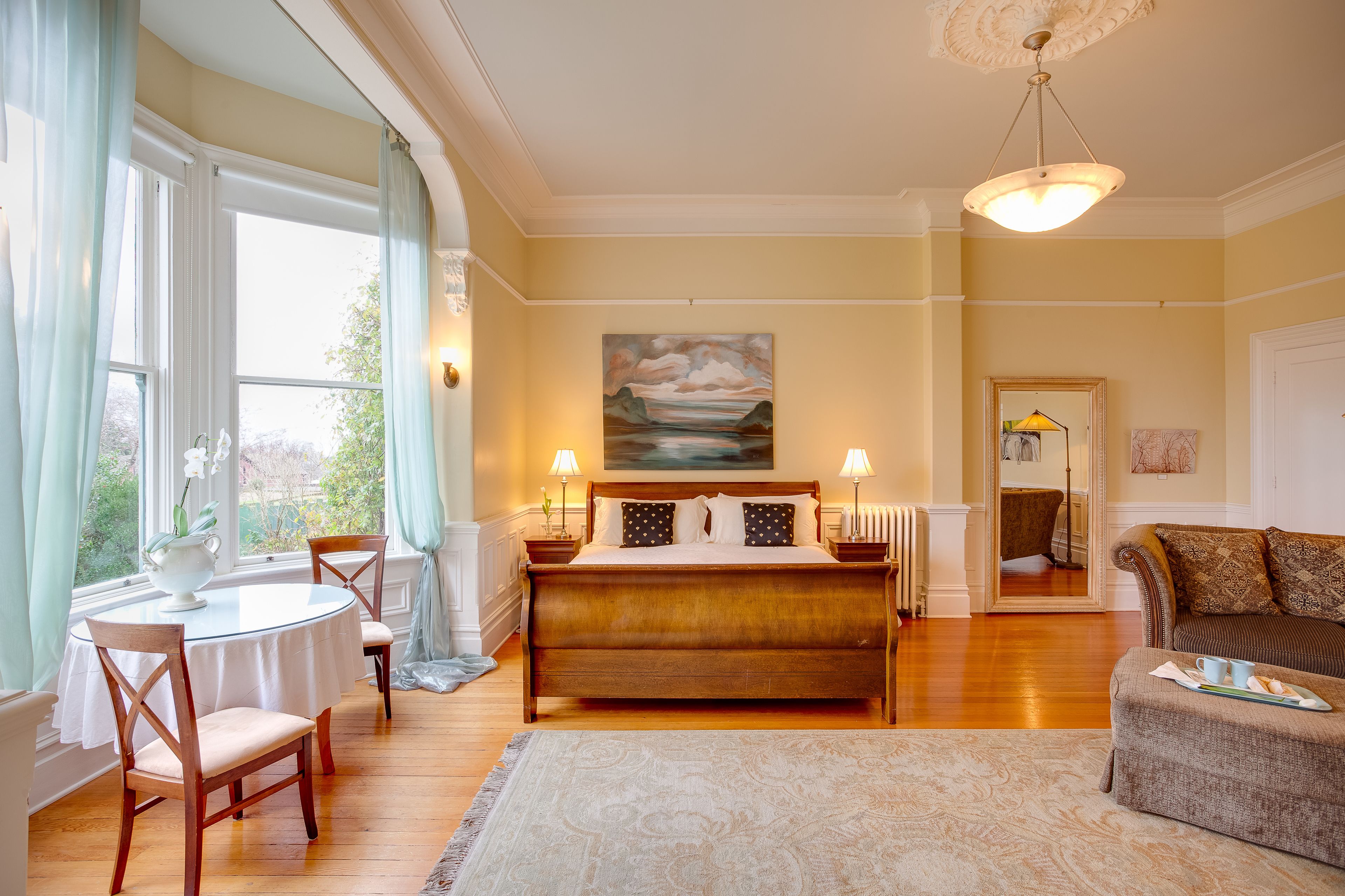 Une chambre avec un grand lit, une table à manger ronde, deux chaises, un canapé et un tableau accroché au mur.