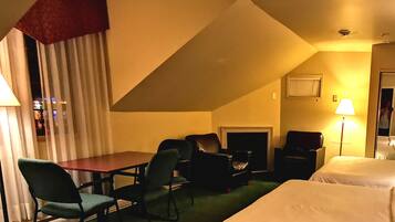 A hotel room with a bed, a desk, two chairs, a fireplace, and a lamp.