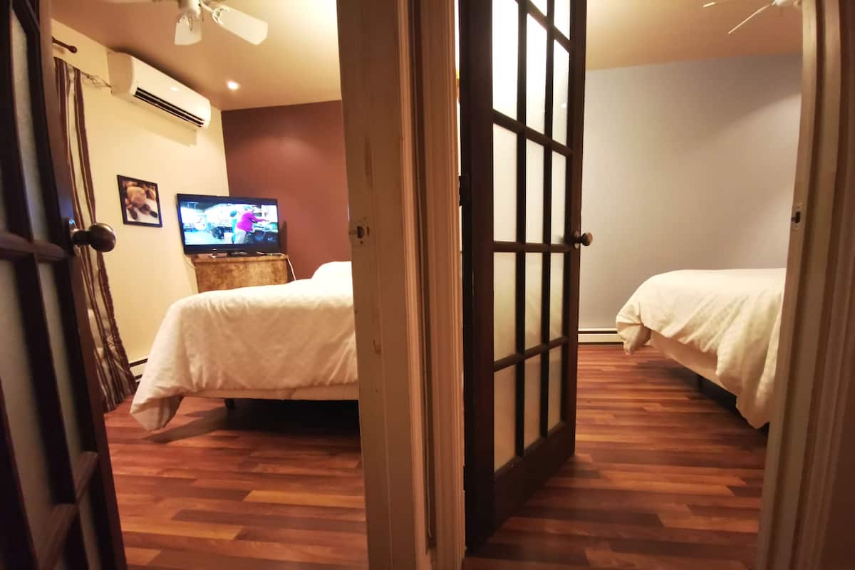 A hotel room with two beds, a television on a wooden stand, and a wooden floor.