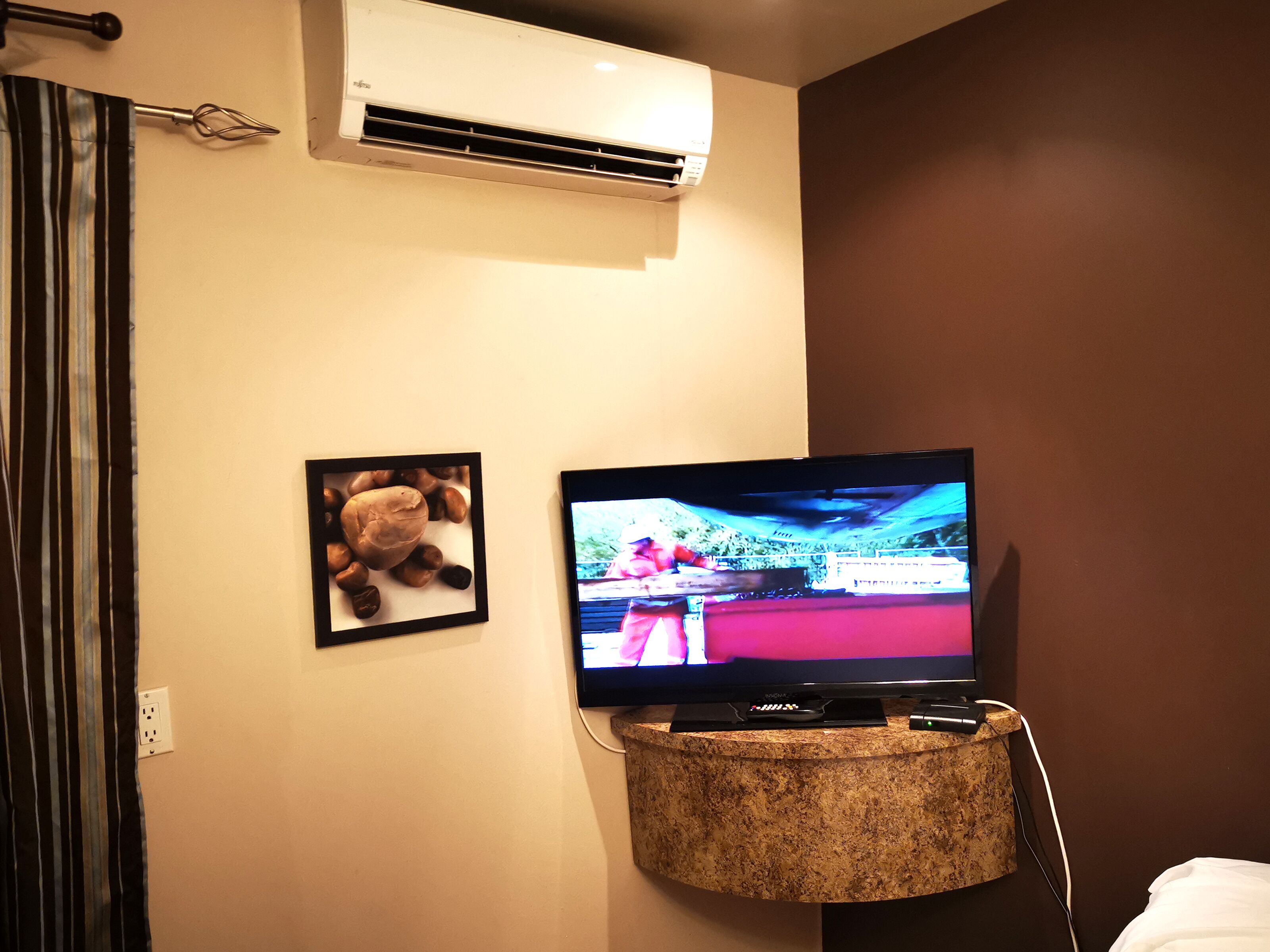 Een kamer met een televisie op een marmeren standaard, een airconditioningunit erboven en een ingelijste foto aan de muur.